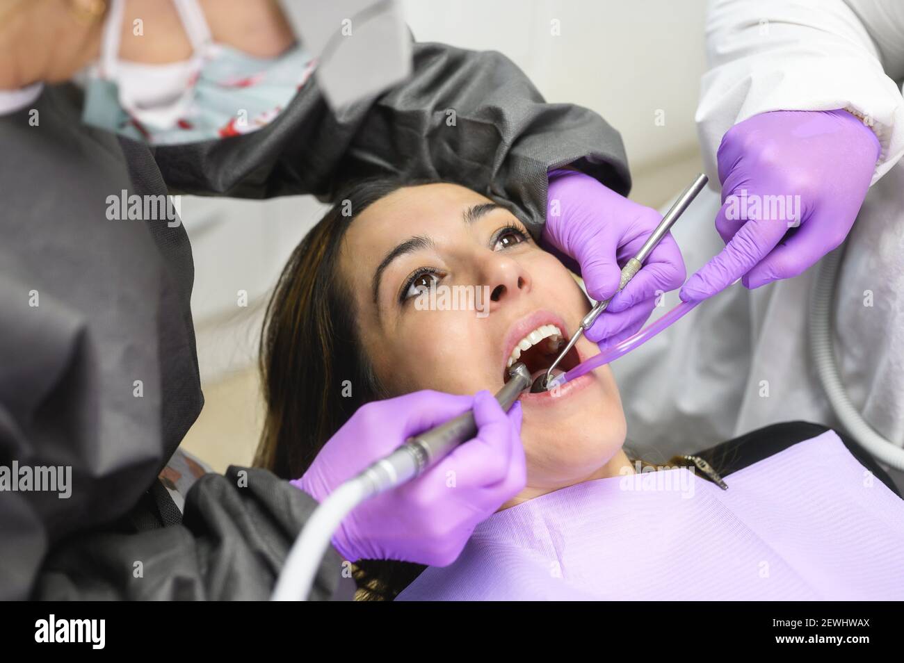 Giovane donna visita ambulatorio odontoiatrico per il trattamento professionale dei denti. Donna dentista si piega sul paziente. Strumento medico per la presa orale Foto Stock