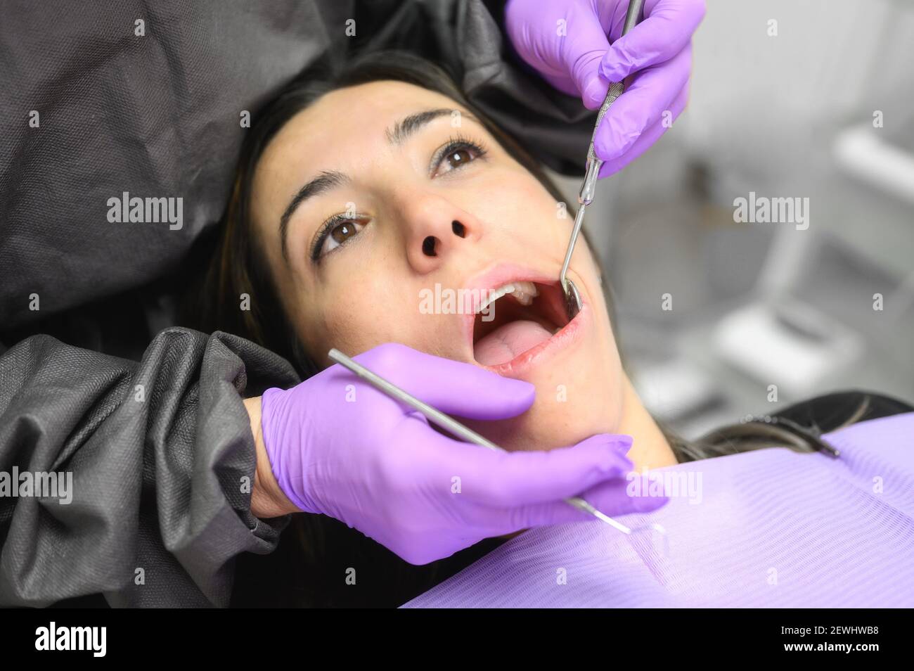 Giovane donna visita ambulatorio odontoiatrico per il trattamento professionale dei denti. Donna dentista si piega sul paziente. Strumento medico per la presa orale Foto Stock