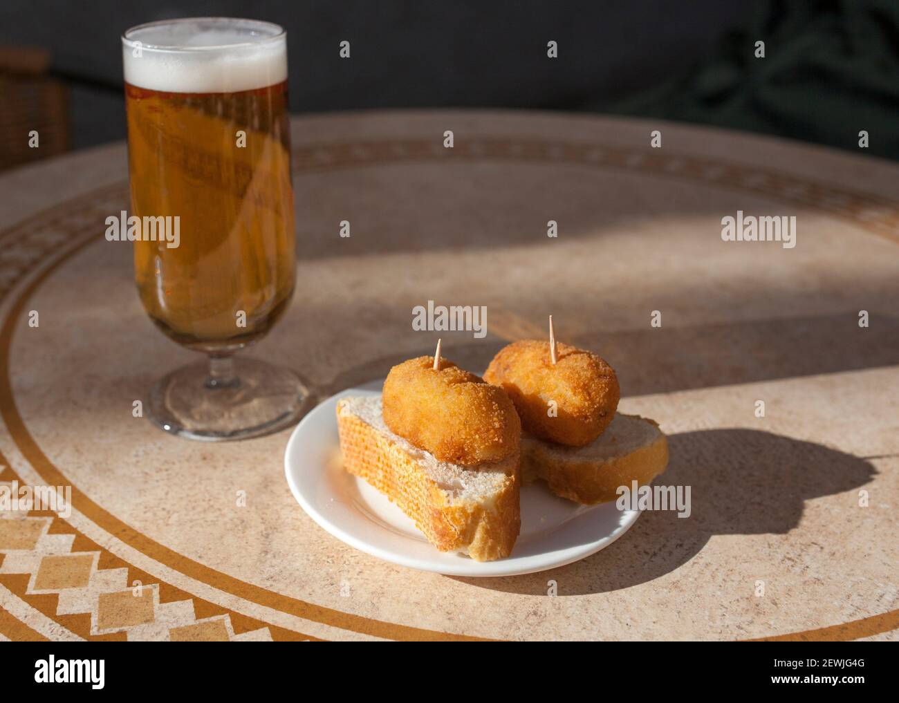 Pinchos spagnoli di crocchette vicino al bicchiere di birra. Pincho servito sul tavolo soleggiato della terrazza. Foto Stock