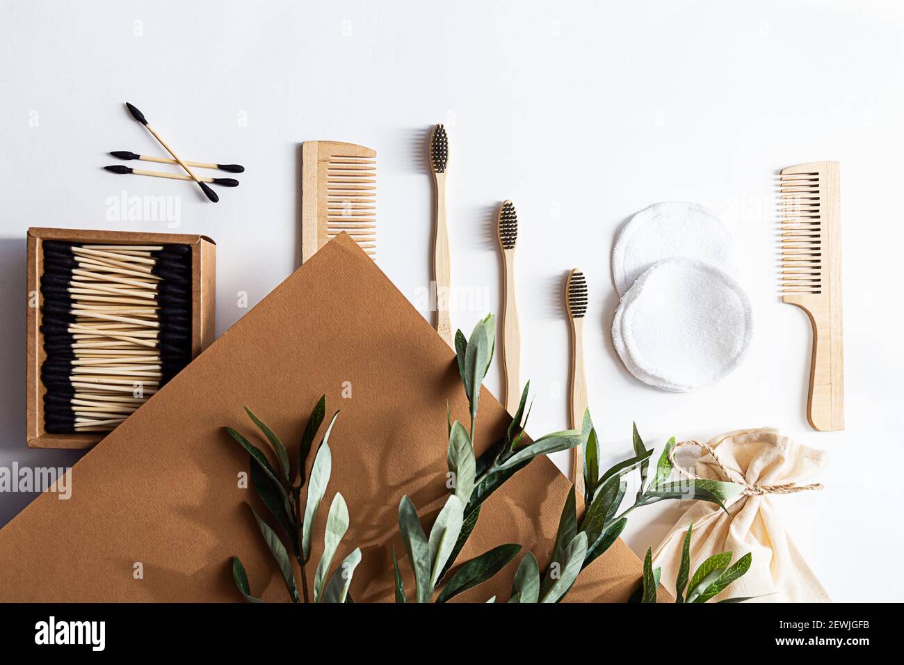 Stile di vita ecocompatibile. Moderna scena di natura morta con ramo di olive, zero rifiuti prodotti per la casa. Spazzolini da denti di bambù e orecchini a bastone, reusa Foto Stock