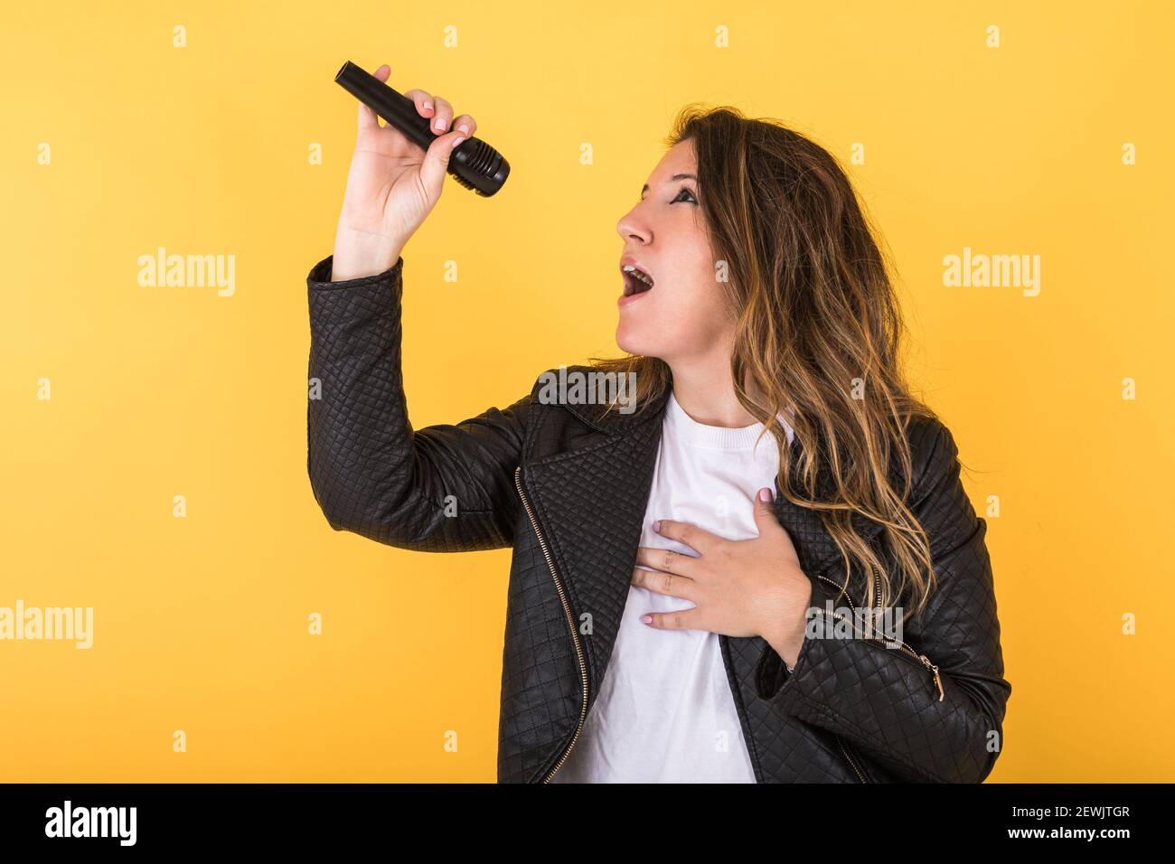 Giovane cantante ragazza con giacca nera in pelle che canta con microfono  su sfondo giallo Foto stock - Alamy