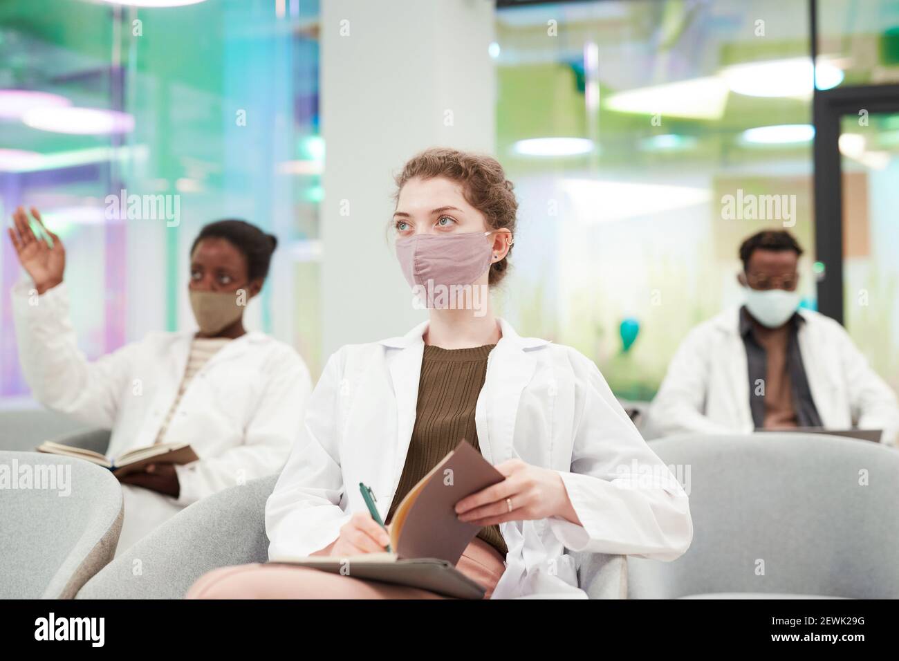 Ritratto di giovane donna che indossa maschera e camice da laboratorio mentre si ascolta la lezione di medicina in università o centro di lavoro, copia spazio Foto Stock