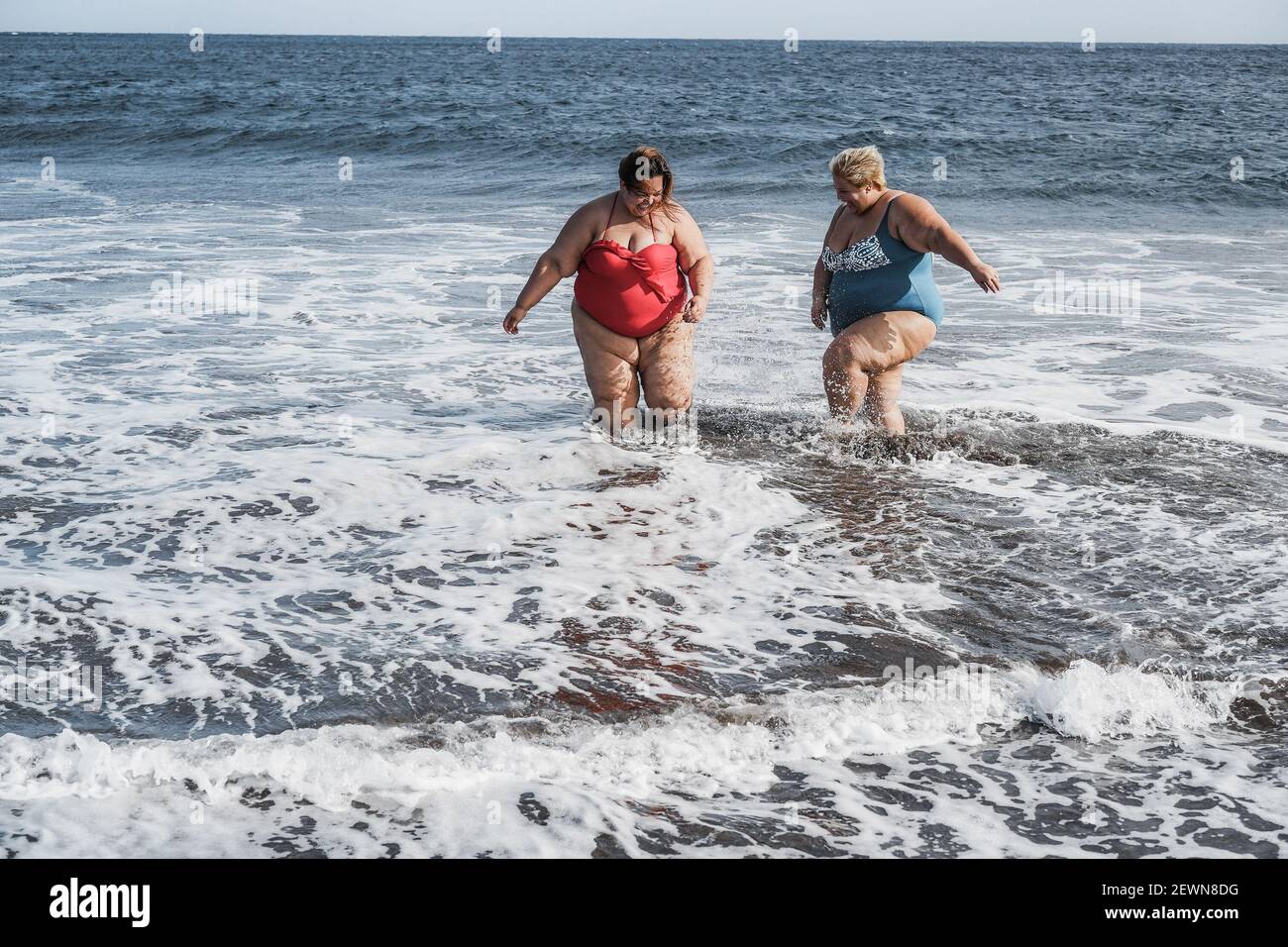 Donne curvy che giocano sulla spiaggia divertendosi in estate Tempo - facce a fuoco Foto Stock