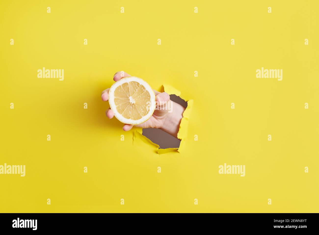 donna mano che tiene vetro con limonata attraverso il foro dentro carta gialla Foto Stock