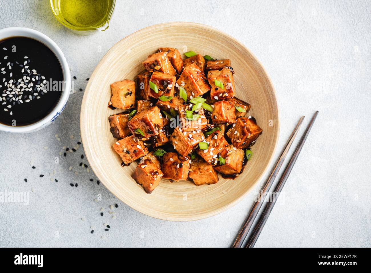 Mescolare il tofu marinato fritto con semi di sesamo, salsa di soia e scalioni in un recipiente, vista dall'alto Foto Stock