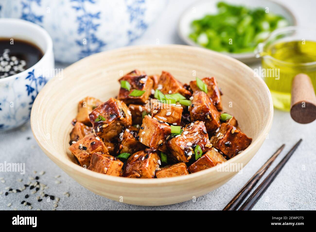 Tofu di teriyaki fritto vegano con scalioni e semi di sesamo in ciotola di bambù. Cucina asiatica Foto Stock