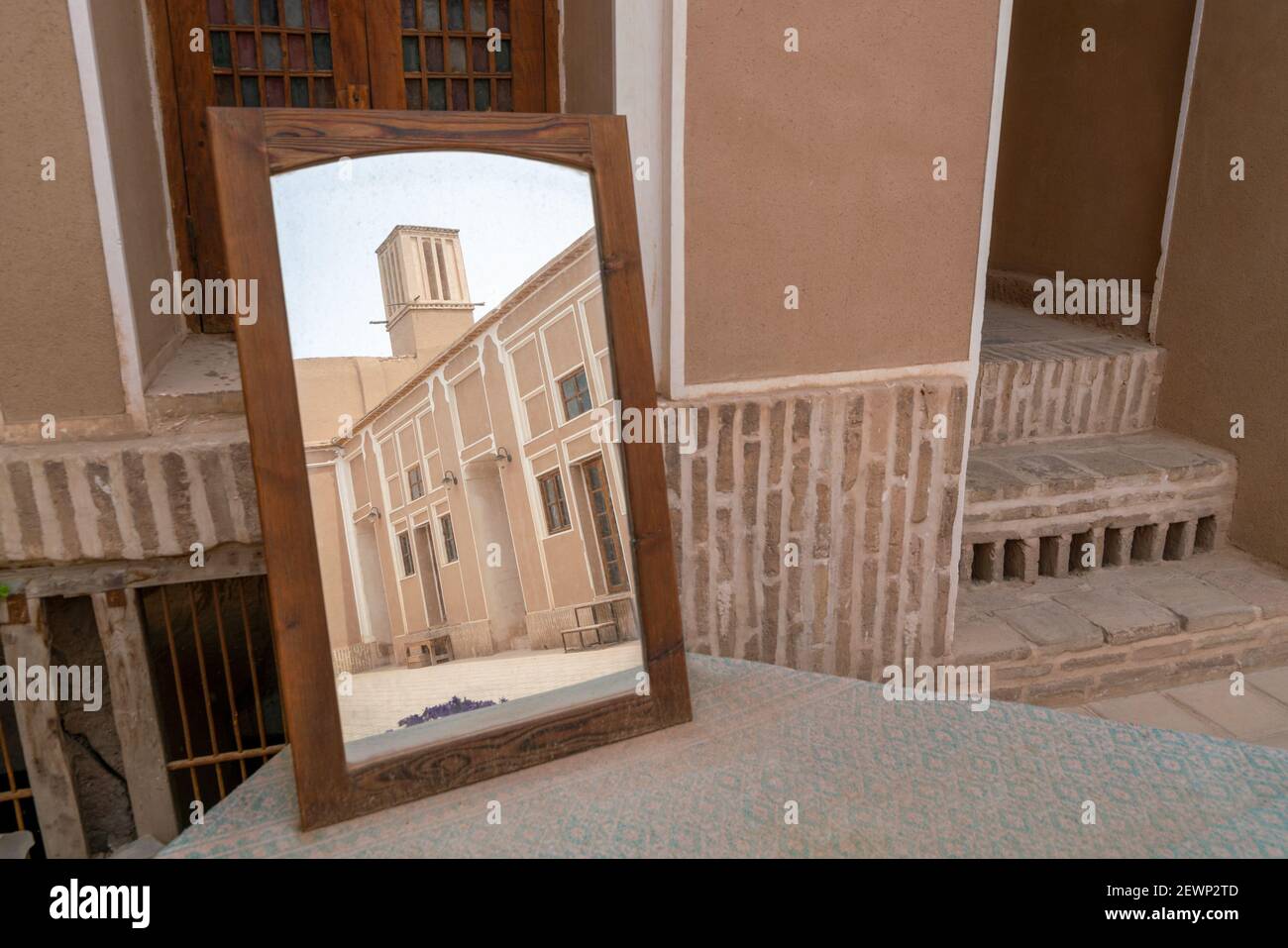 La torre del vento, dispositivo di raffreddamento medievale, si riflette in uno specchio in piedi su un tavolo nelle strade di Yazd, Iran. Foto Stock