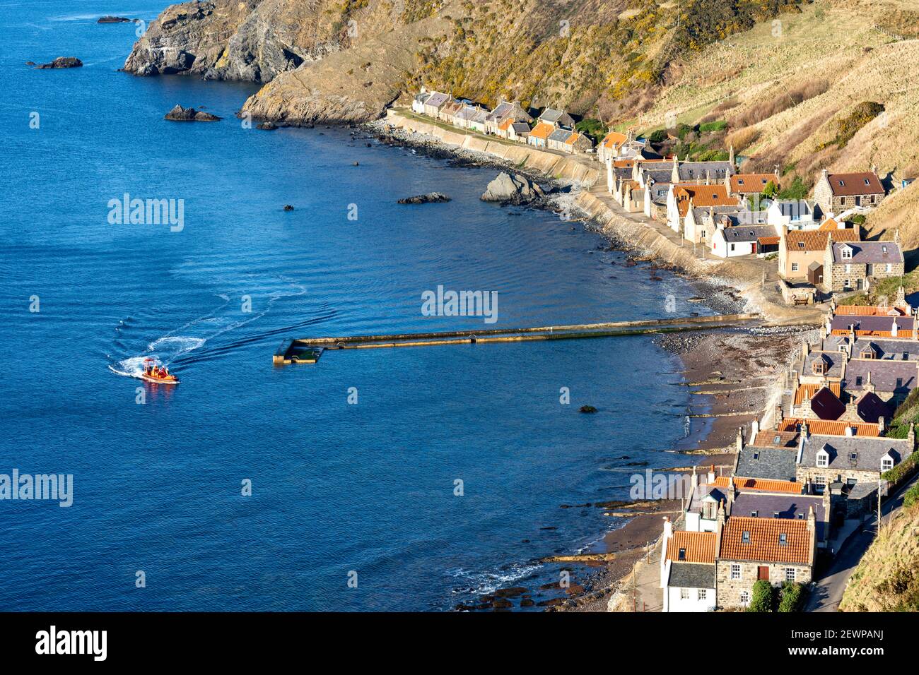 CROVIE VILLAGGIO ABERDEENSHIRE SCOZIA UNA FILA DI CASE TETTO ROSSO PIASTRELLE E UNA BARCA ARANCIONE VICINO AL MOLO Foto Stock