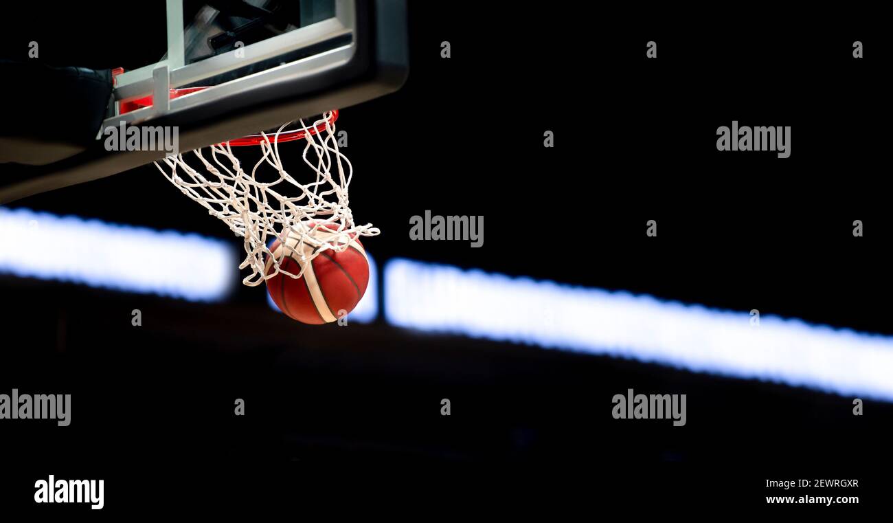 La palla da basket arancione vola attraverso il cesto. Sfondo sportivo per la visualizzazione del prodotto, banner o mockup Foto Stock