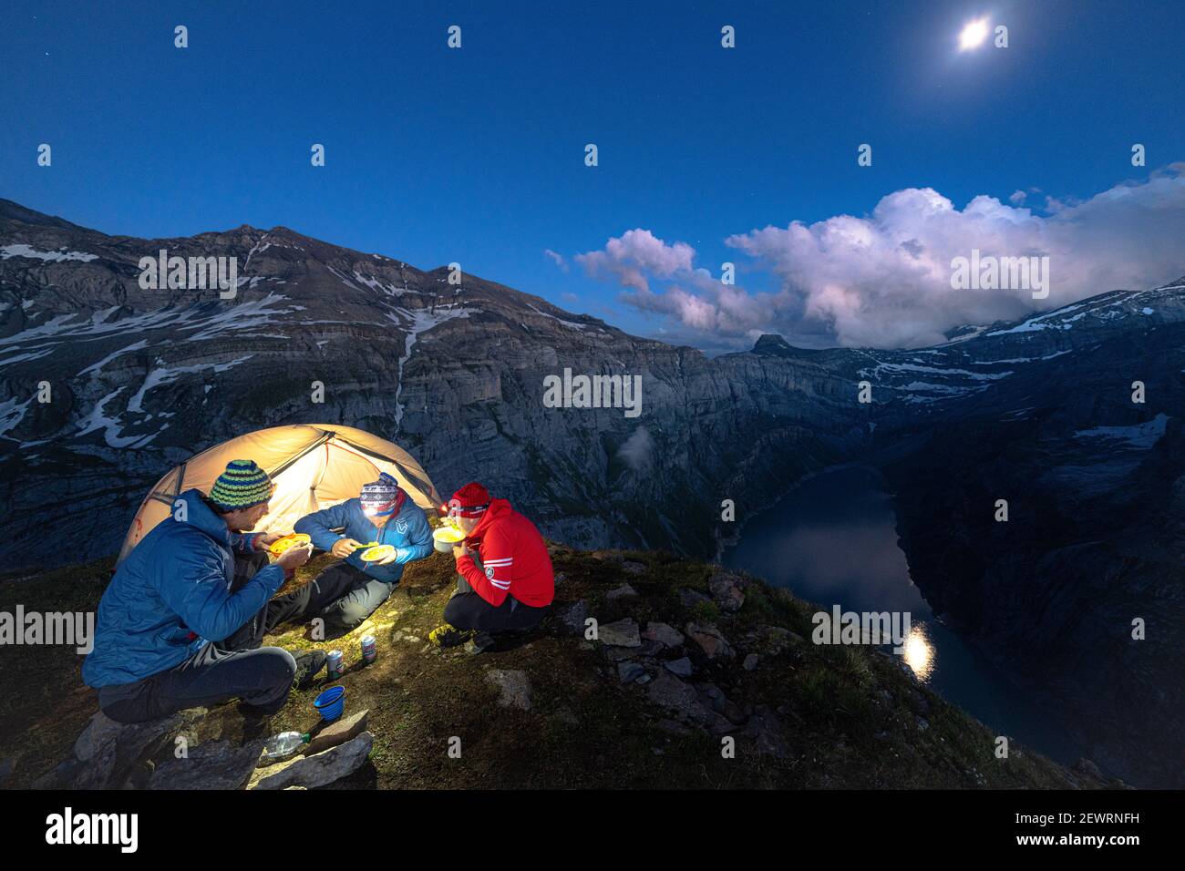 Tre uomini escursionisti godendo cena fuori una tenda sopra il lago Limmernsee al crepuscolo, Canton Glarona, Svizzera, Europa Foto Stock