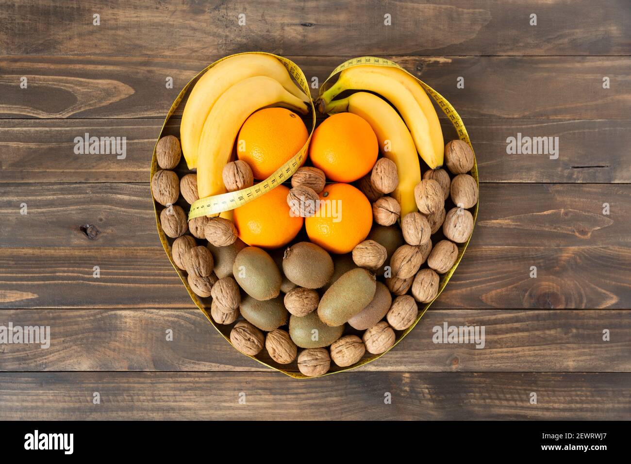 Vista dall'alto di frutta assortita e frutta secca che formano un cuore su uno sfondo di legno scuro. Concetto di alimentazione sana e benessere. Spazio per il testo. Foto Stock