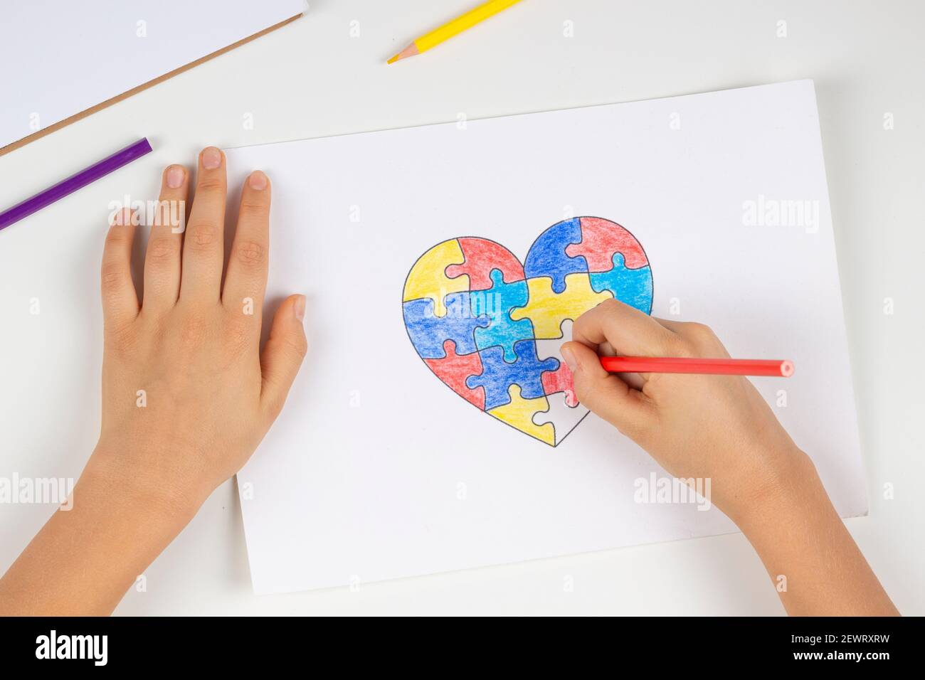 Bambino mani colorazione cuore puzzle con matite colorate. Vista dall'alto. Concetto di giorno di consapevolezza autismo mondiale Foto Stock
