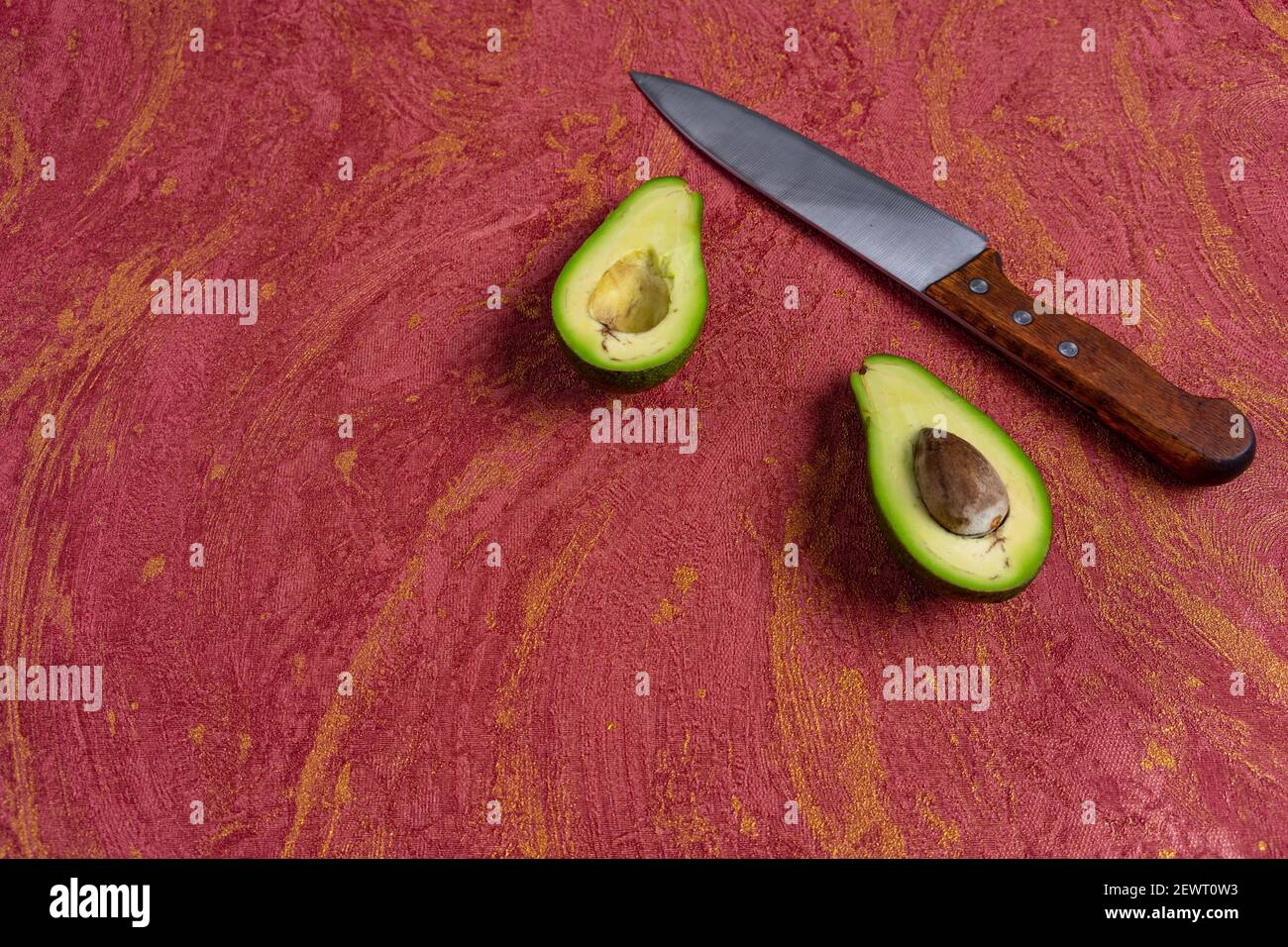 Viso avocado. Avocado tagliato al centro e coltello su sfondo rosso. Varietà avocado vista dall'alto Foto Stock