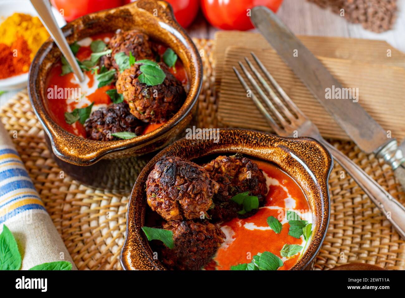 piatto vegano con zuppa di tomatoe piccante orientale e noci lenticchie polpette servite in rustiche ciotole marroni ricoperte di latte di cocco Foto Stock