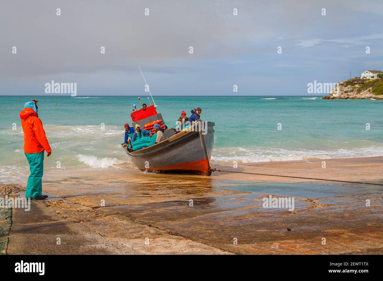 Pescatori vestiti con colori che abbelliscono la loro barca al porto di pescatori locale ad Arniston, provincia del Capo Occidentale, Sud Africa Foto Stock