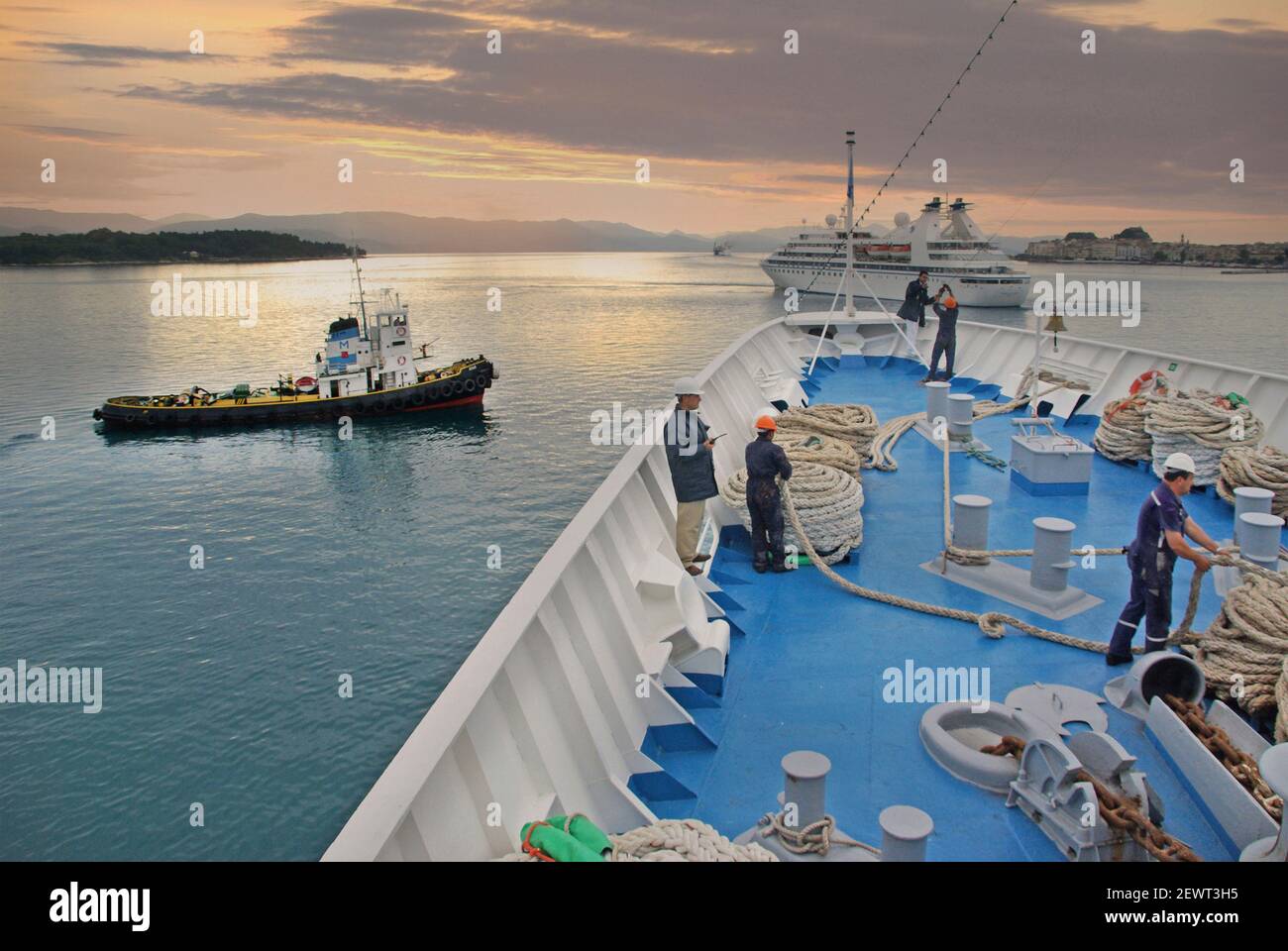 Tug barca Merchant Navy Shipping & marinaio al lavoro prua della nave da crociera bordo ponte equipaggio che lavora la corda falchi giù per porto molo ormeggiatori isola greca Corfu Foto Stock
