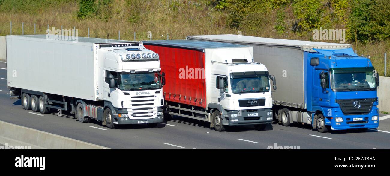 Gruppo di tre viste frontali e laterali sfalsate di colore rosso bianco e il trasportatore della catena di fornitura hgv blu trasporta autocarri revisione camion Autostrada a quattro corsie Inghilterra Regno Unito Foto Stock