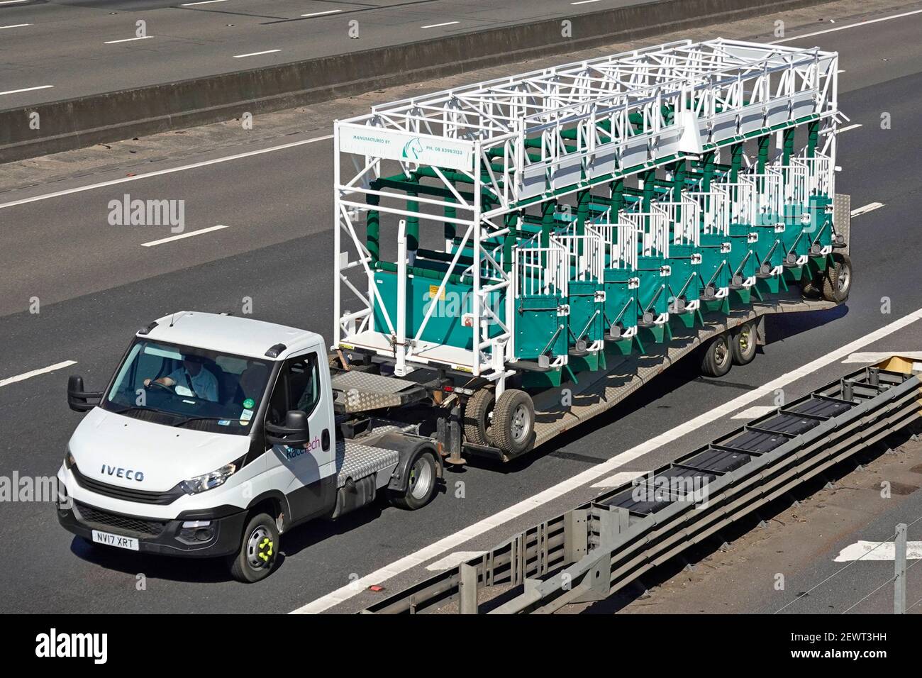 Vista aerea del piccolo autocarro Iveco e del caricatore articolato basso rimorchio con carico insolito di corse di cavalli portatili gommati cancelli sull'autostrada del regno unito Foto Stock