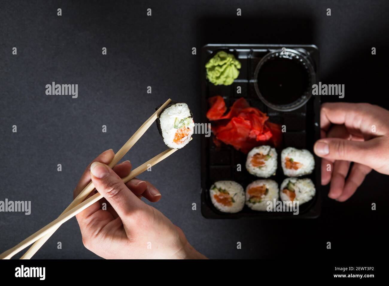 mani di donna che raccolgono il rotolo di sushi dalla scatola, su sfondo nero. Foto Stock