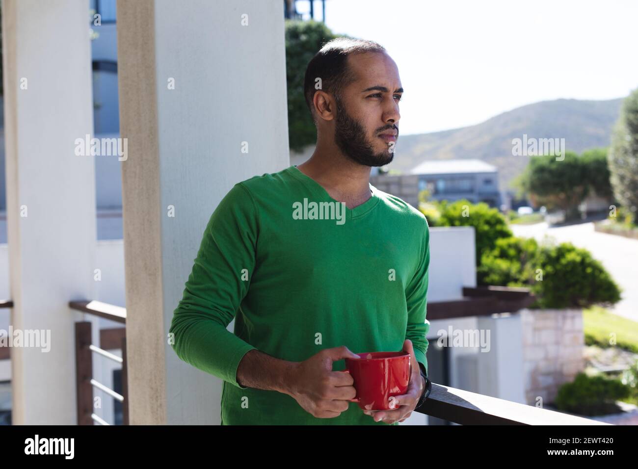 Premuroso uomo da corsa misto che beve una tazza di caffè sul balcone al sole, vista mozzafiato Foto Stock