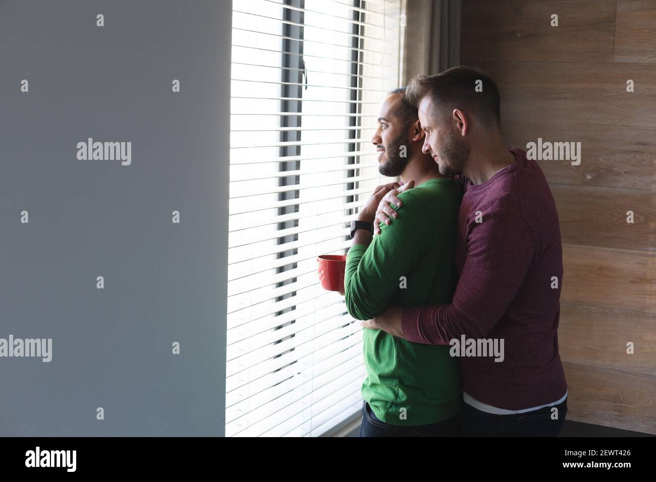 Multi etnica gay maschio coppia bere caffè, sorridente e abbracciare a casa Foto Stock
