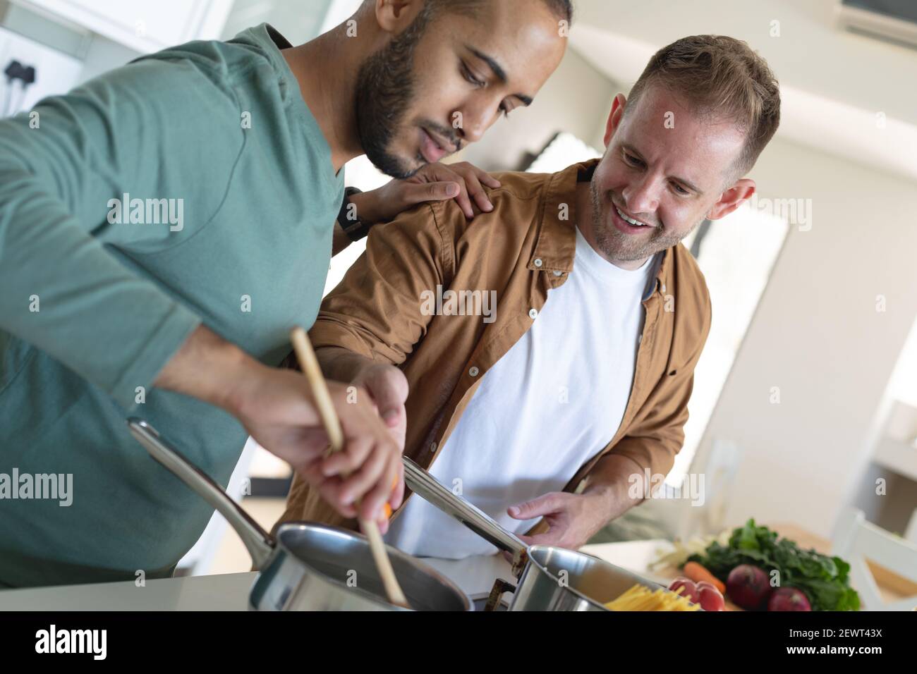 Multi etnica gay maschio coppia sorridente e preparare insieme il cibo a casa Foto Stock