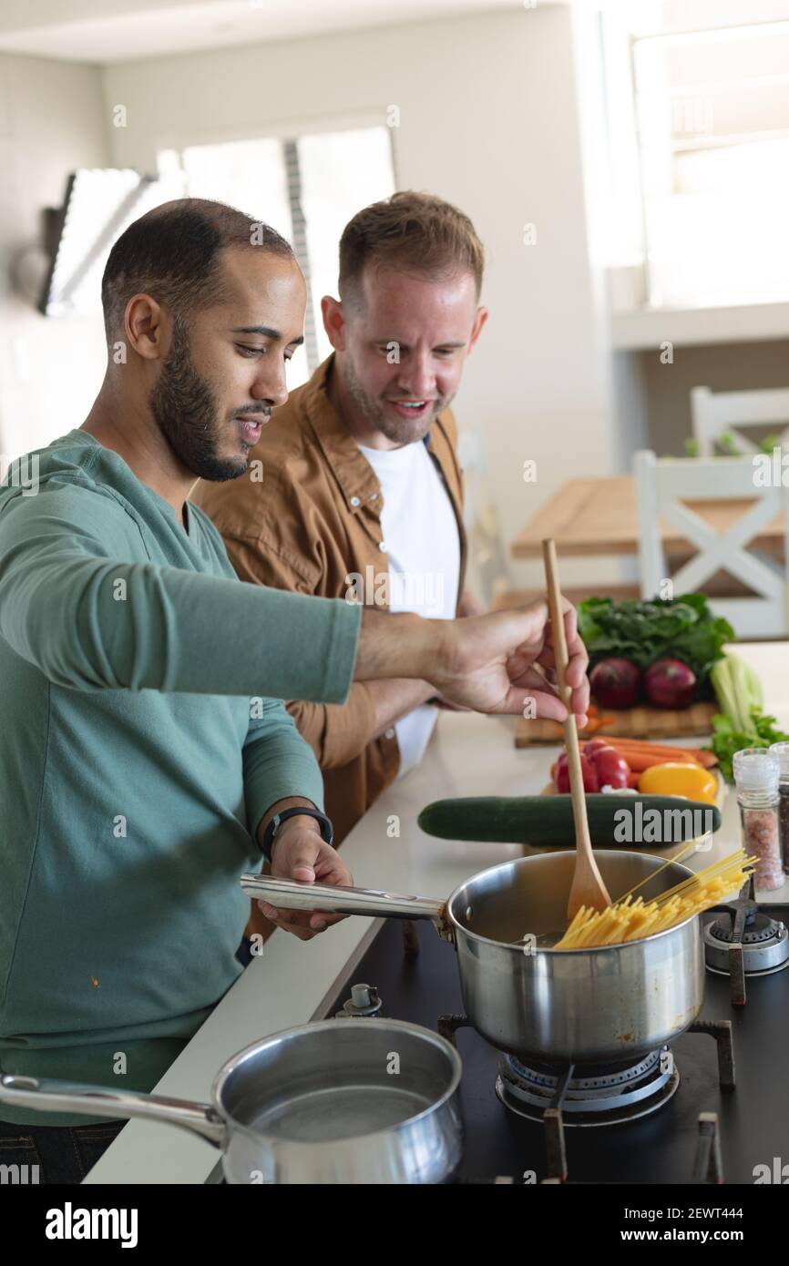 Multi etnica gay maschio coppia sorridente e preparare insieme il cibo a casa Foto Stock