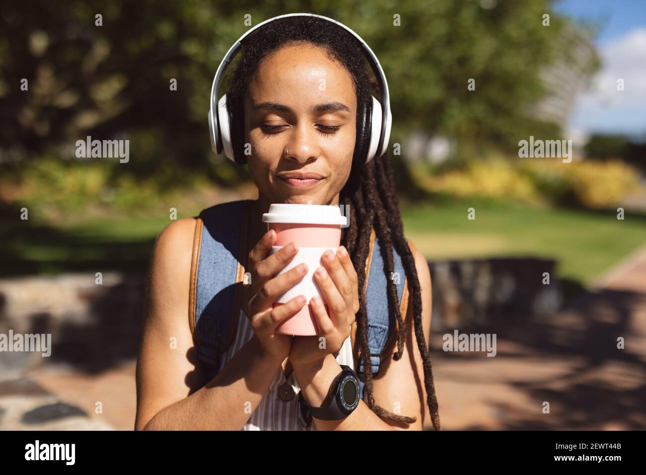 Donna afroamericana sorridente che indossa le cuffie seduti a bere caffè parcheggio Foto Stock
