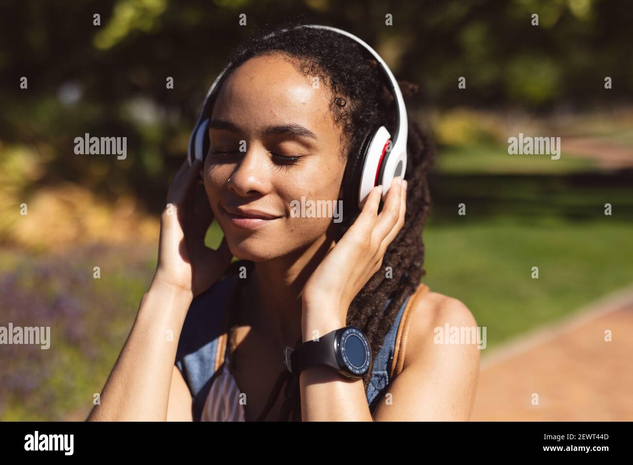 Donna afroamericana sorridente che indossa le cuffie in piedi sull'ascolto dello scooter alla musica in strada Foto Stock