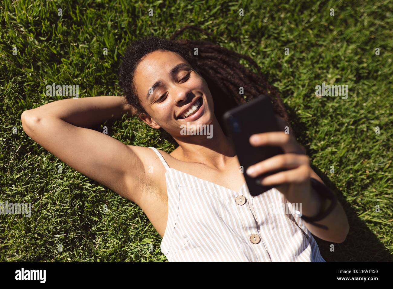 Sorridente afroamericana sdraiata sull'erba e usando un smartphone in parcheggio Foto Stock