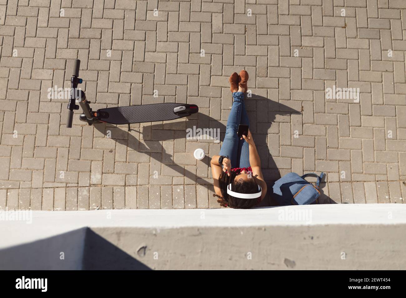 Donna afroamericana che si rilassa, seduta sul pavimento appoggiato al muro e utilizzando uno smartphone Foto Stock