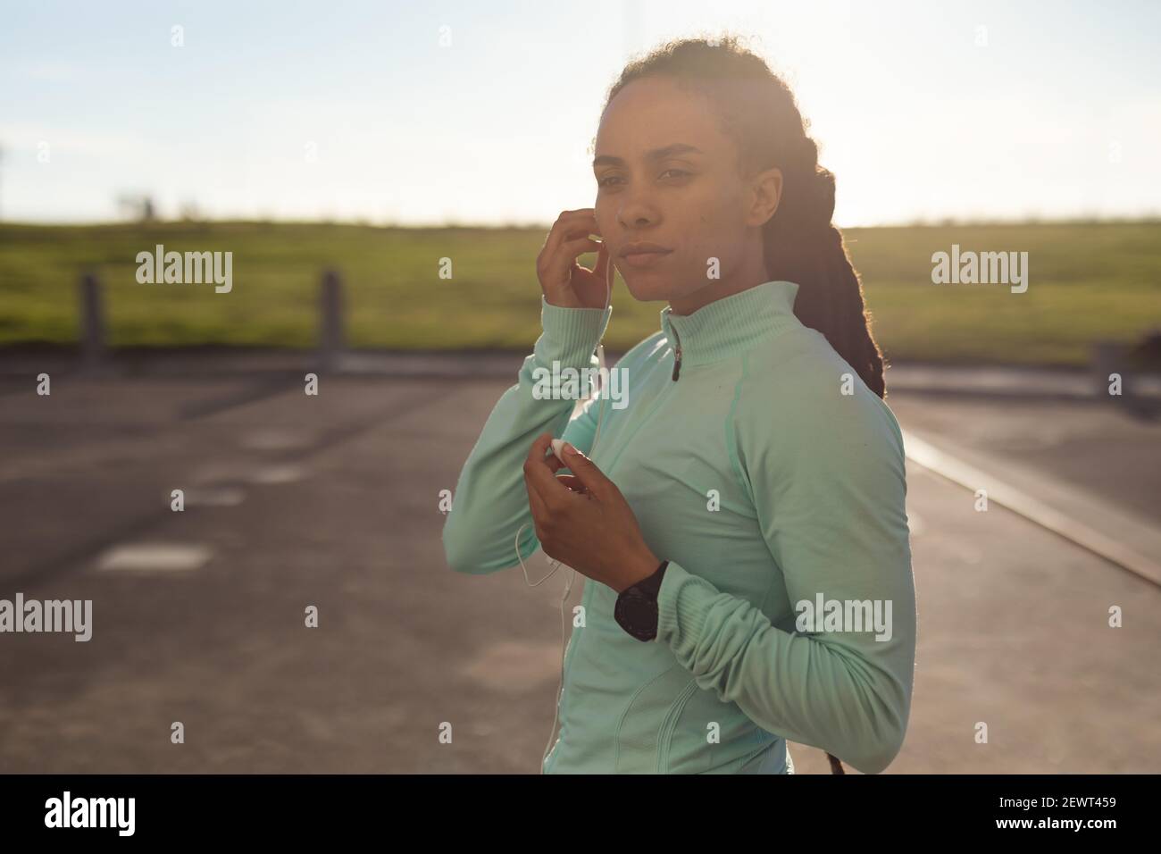 Donna afroamericana che si concentra, indossando abiti sportivi che si esercitano nel parco mettendo gli auricolari in Foto Stock
