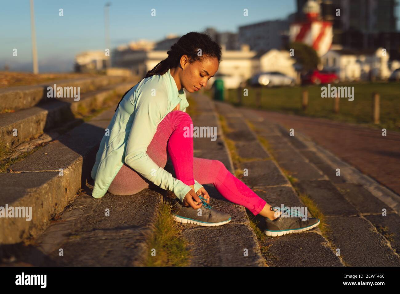 Donna afroamericana che indossa abiti sportivi che si esercitano in strada urbana pattino di legatura Foto Stock