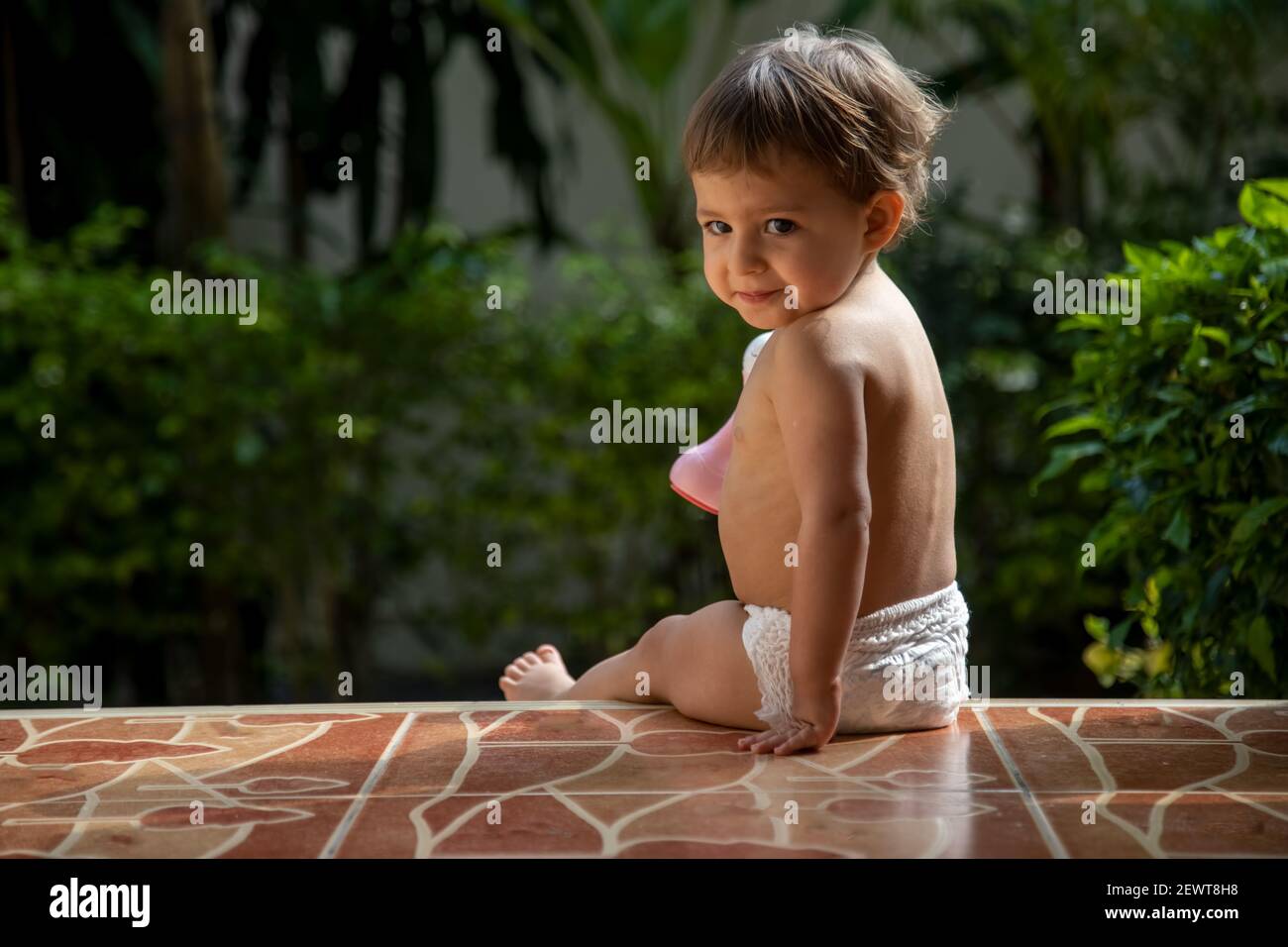 un affascinante bambino si siede sui gradini di una casa sotto la luce del sole. vista posteriore Foto Stock