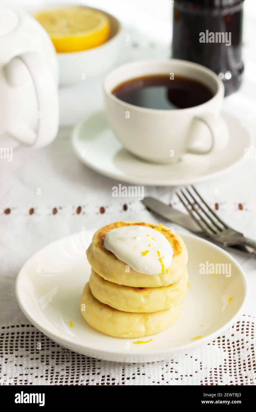 Frittelle al formaggio con panna acida e scorza di limone, servite con tè. Foto Stock