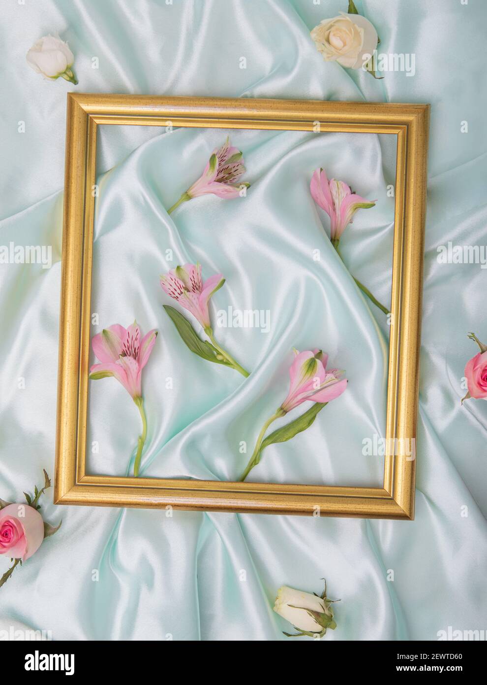 Cornice dorata in cima al raso blu con rose e fiori rosa primavera. Concetto di molla piatta. Foto Stock
