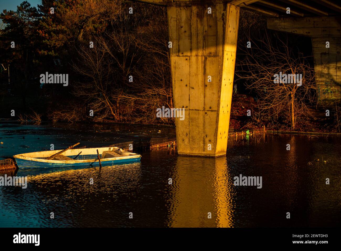 La barca fu abbandonata sotto il ponte, alla luce del tramonto sul lago Foto Stock