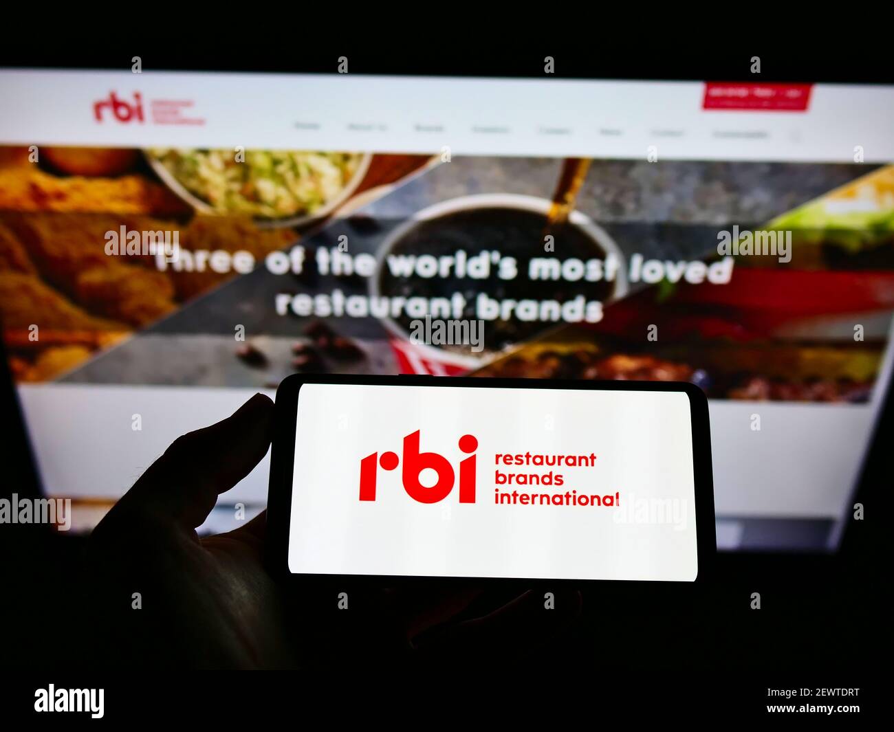 Persona che tiene il cellulare con il logo della società di fast food Restaurant Brands International Inc. (RBI) su schermo con il sito web. Mettere a fuoco il display del telefono. Foto Stock