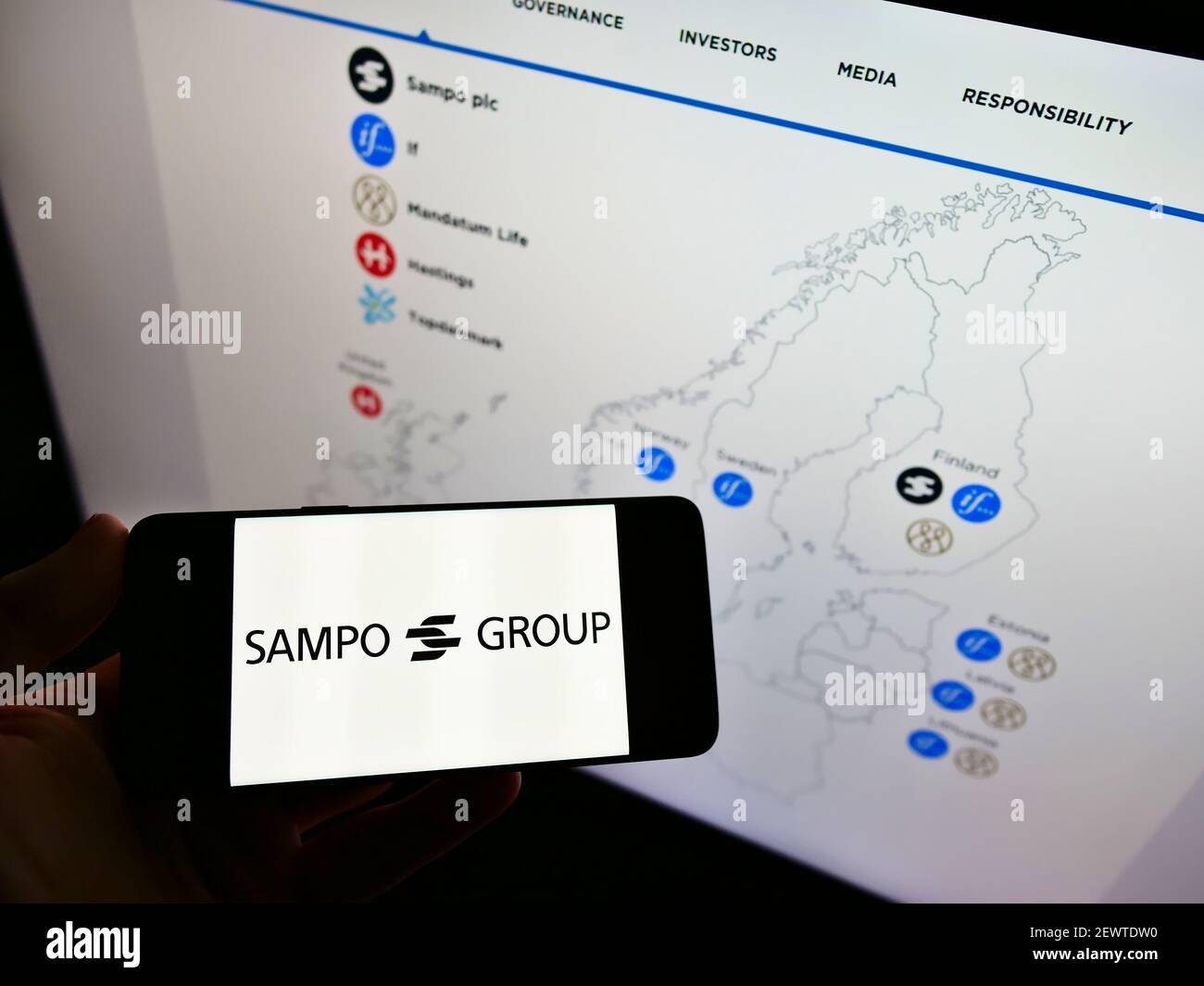 Persona titolare cellulare con logo della società finlandese di servizi finanziari Sampo Oyj su schermo davanti alla pagina web con mappa. Mettere a fuoco il display del telefono. Foto Stock