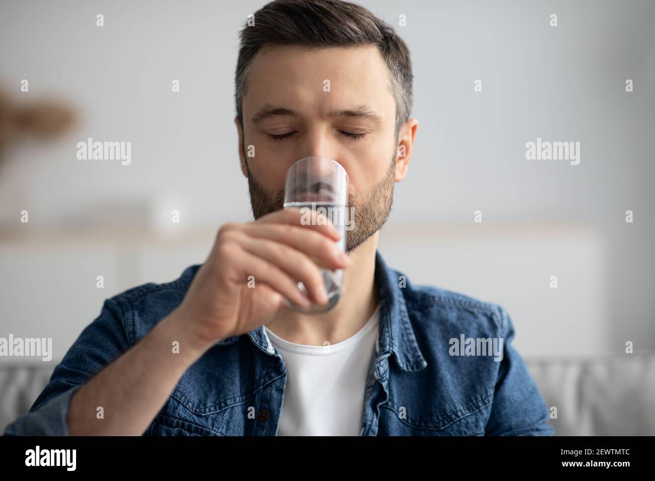 Primo piano di un uomo di mezza età che beve acqua a casa Foto Stock