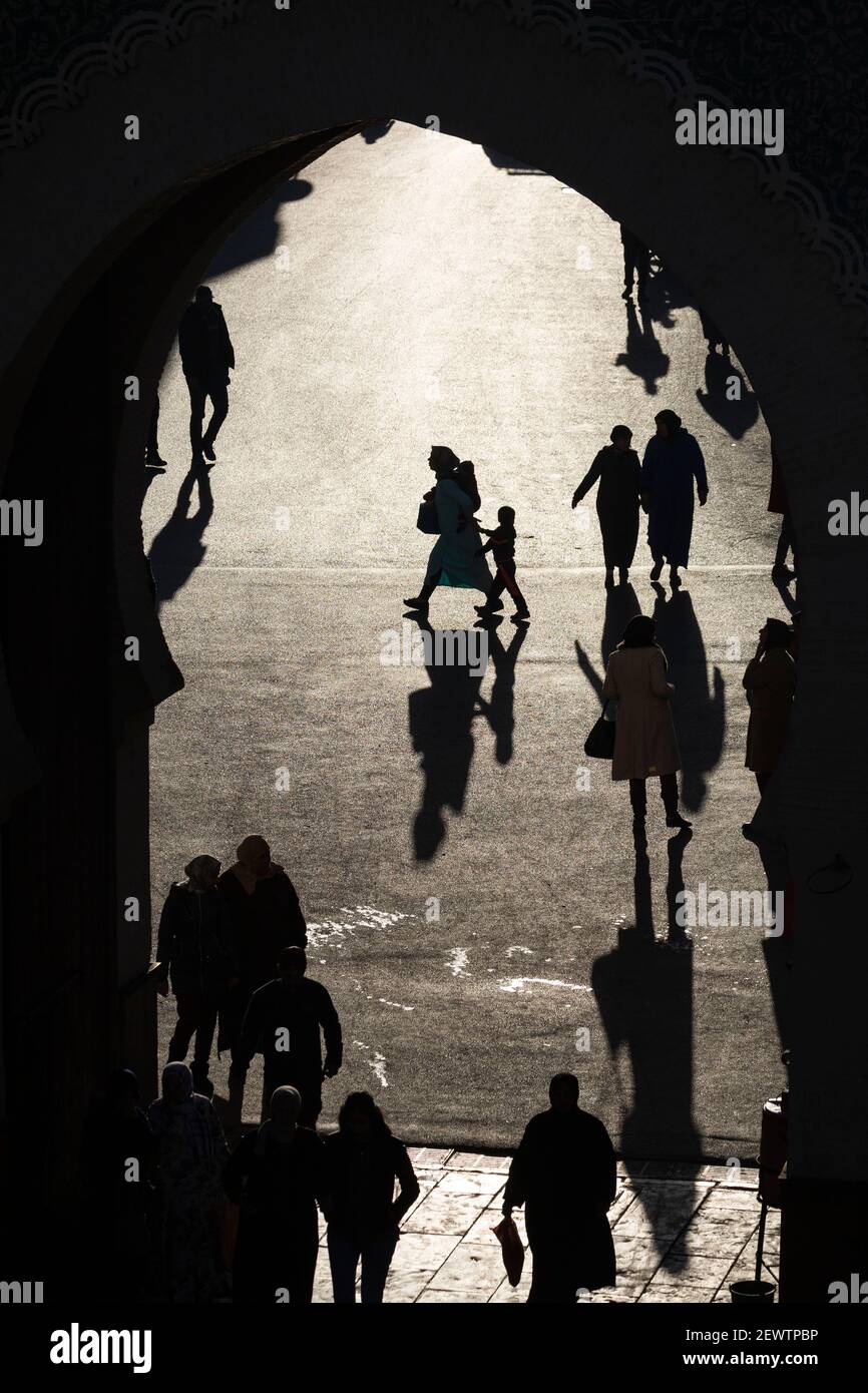Vista attraverso la porta Blu (Bab Bou Jeloud) di pedoni che gettano lunghe ombre sul terreno, Fes, Marocco Foto Stock