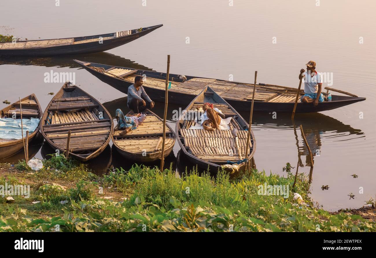 I pescatori riposano sulle loro barche vicino ad una riva del fiume al tramonto. Fotografia scattata in un distretto rurale nel Bengala occidentale, India Foto Stock