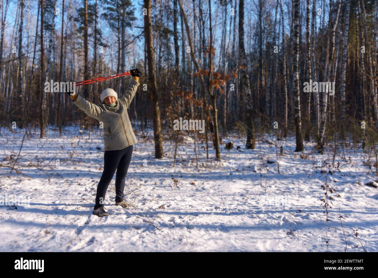 Donna anziana che fa esercizio con bastoni per nordic walking dentro foresta invernale Foto Stock