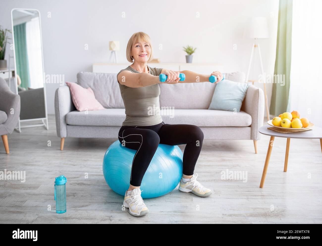Bella donna matura seduta su palla fitness, allenandosi con manubri nella  sua palestra di casa, spazio vuoto. Stile di vita attivo Foto stock - Alamy