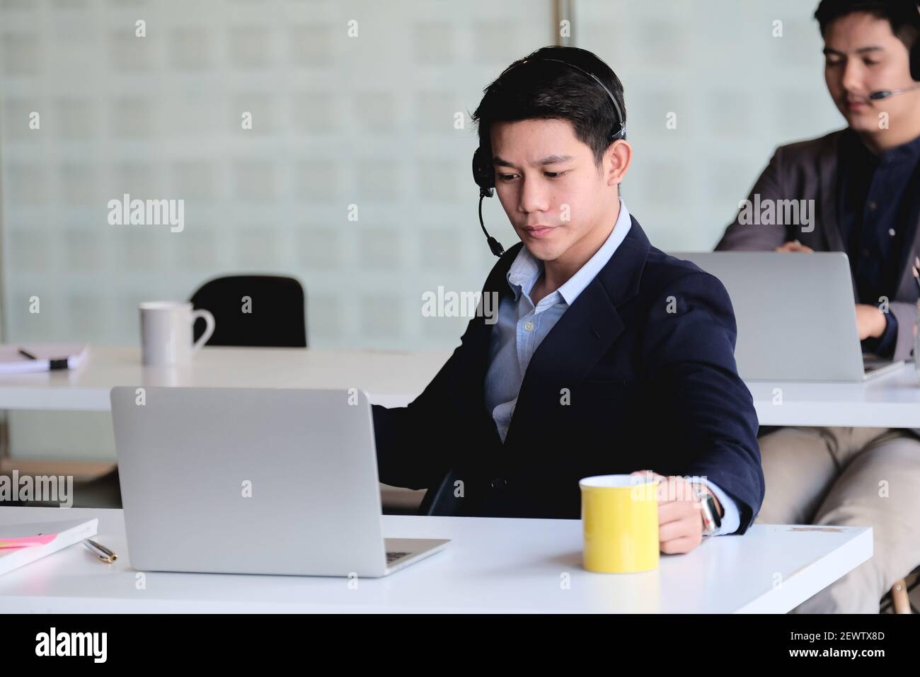 Uomo d'affari asiatico in cuffia che guarda il laptop, guarda un buon webinar, consulente del cliente, imparare a distanza lingue, prendere appunti, uomo felice Foto Stock