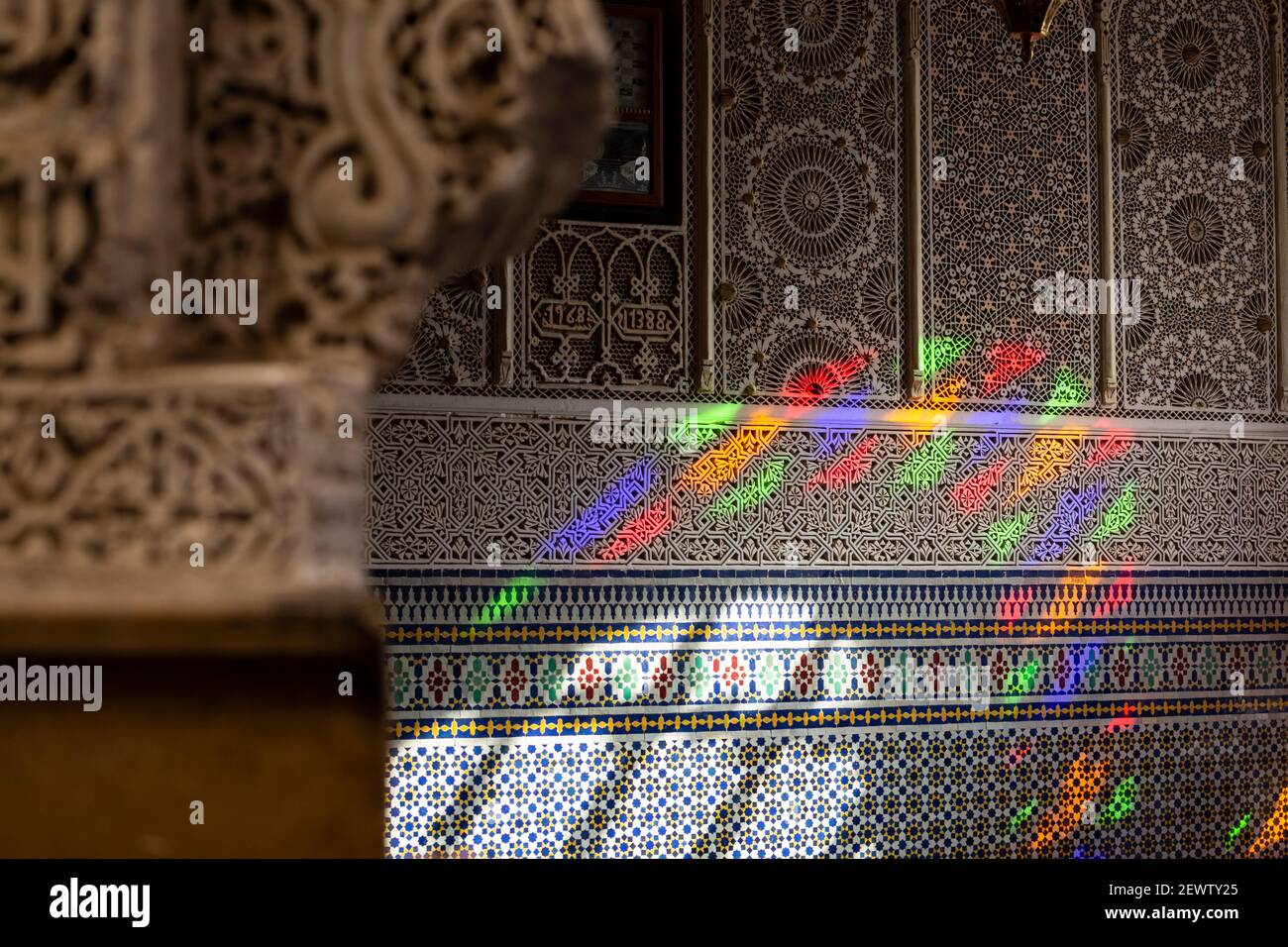 Luce colorata da una finestra in vetro colorato proiettata sulle intricate pareti disegnate da una moschea nella medina di Fes, Marocco Foto Stock