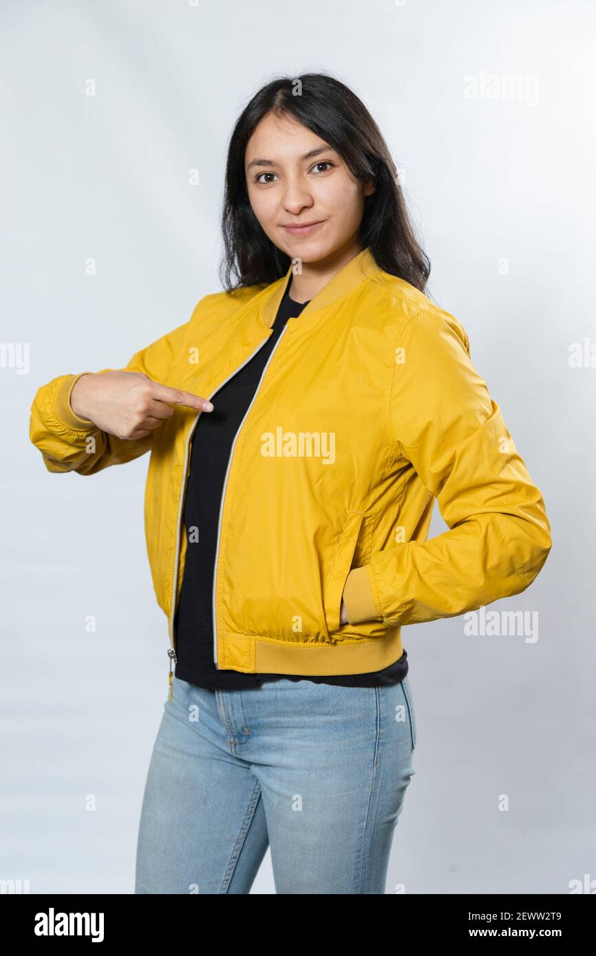 Bombardiere giallo da donna mockup-Ritratto di giovane donna ispanica indicando sulla sua giacca su sfondo bianco Foto Stock