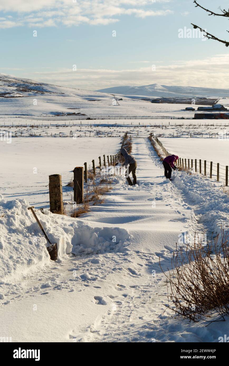 Madre e figlia che scovano la neve dal vialetto, Orkney Isles Foto Stock