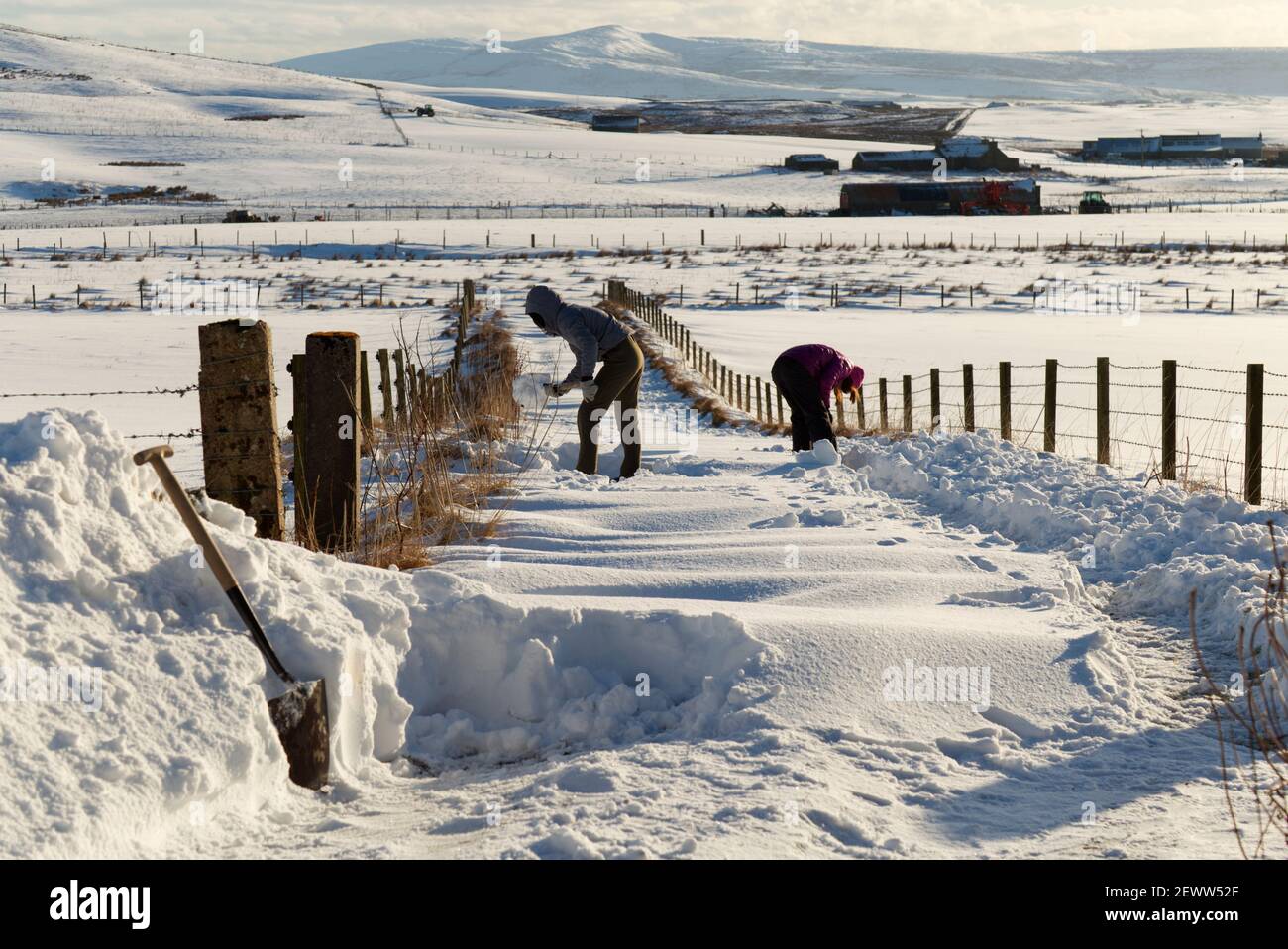 Madre e figlia che scovano la neve dal vialetto, Orkney Isles Foto Stock