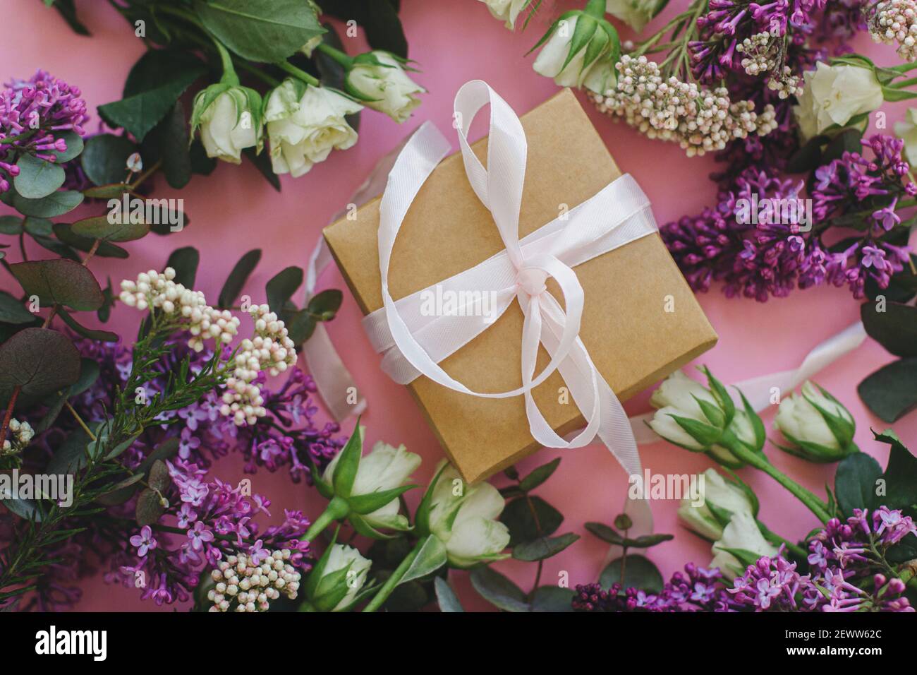 Semplice confezione regalo con nastro e bella lilla e rose cornice piatta posare su sfondo rosa brillante. Giorno felice delle madri o giorno delle donne, elegante colorato Foto Stock